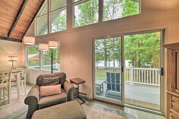 A spacious room with a large sliding glass door leading to an outdoor deck, a cozy seating area with a sofa and ottoman, and a small table.