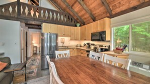 A spacious kitchen with wooden cabinets, a large dining table, and a view of the outdoors. - Cozy Maine Lakefront Escape Fall Foliage & Fire (Limerick)