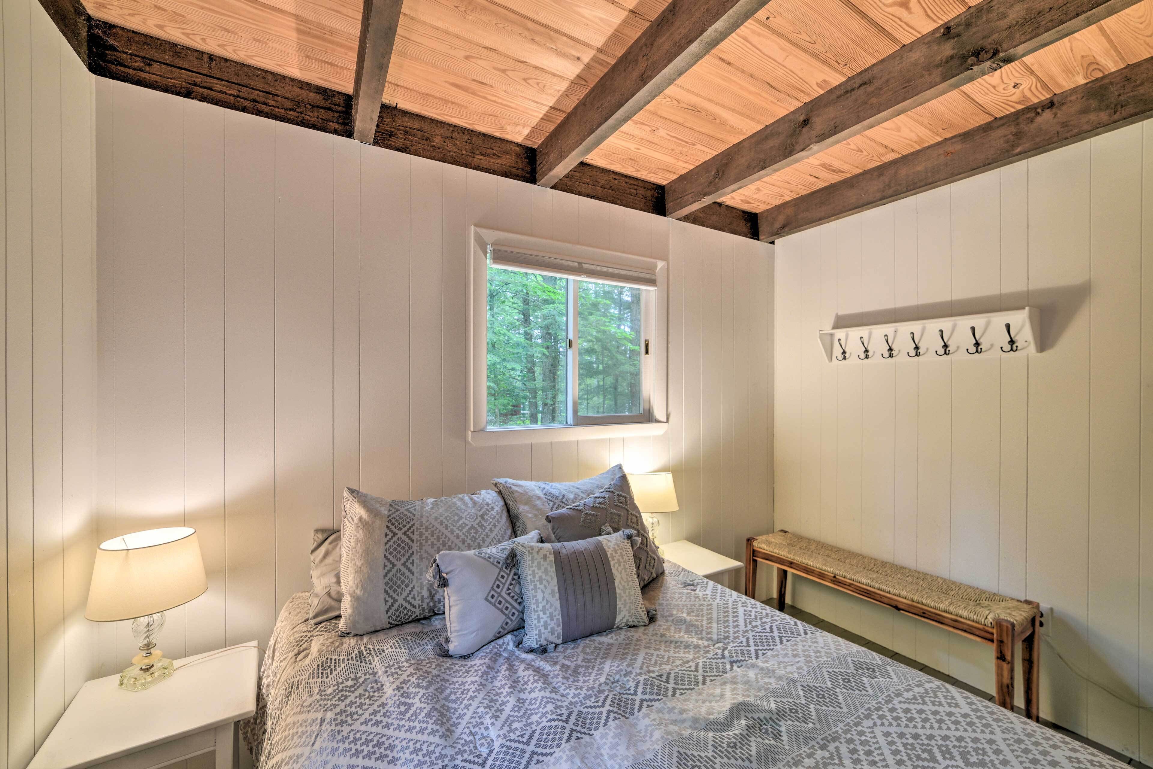 A bedroom with a bed, bedside lamps, a window, a bench, and a coat rack.