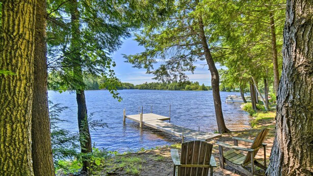 A lakeside view with a dock extending into the water, surrounded by trees and a wooden chair. - Maine Lakefront Escape: Dock, Watercraft, Fire Pit (Limerick)