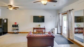 A living room with a large flat-screen TV, ceiling fans, a sofa, a coffee table, and a dining area with a table and chairs.