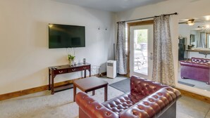 A living room with a leather sofa, a TV mounted on the wall, a small table, and a window with curtains. - Lava Hot Springs Studio w/ Views, Walk to River (Lava Hot Springs)