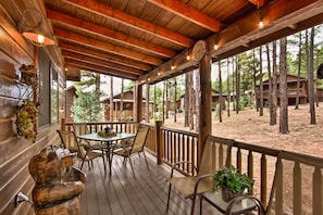 Um deck de madeira com mesa e cadeiras, cercado por um guarda-corpo de madeira, com vista para uma área arborizada com cabanas.