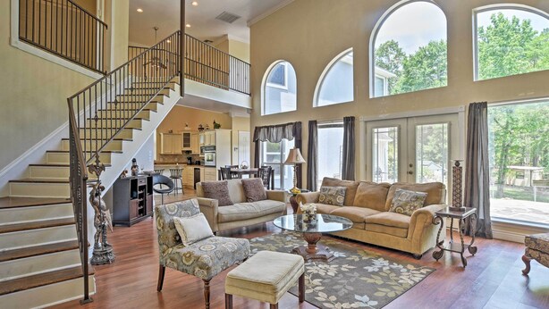 A spacious living area with a staircase, a dining area, and large windows offering views of the outdoors. - Cozy Lakefront Benton Home ~ 20 Mi to Shreveport! (Benton)