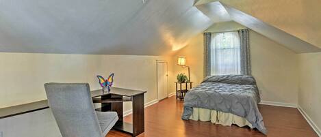 A bedroom with a bed, a desk, and a chair. There is a ceiling fan and a window with curtains.