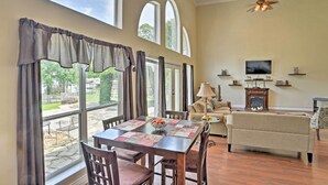 A spacious living room with a dining area, large windows, a ceiling fan, a television, and a fireplace. - Cozy Lakefront Benton Home ~ 20 Mi to Shreveport! (Benton)