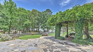 A stone patio with a grassy area and trees in the background. - Cozy Lakefront Benton Home ~ 20 Mi to Shreveport! (Benton)