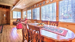 A wooden interior with a dining table, chairs, and a window with blinds.