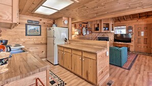 A wooden cabin interior with a kitchen featuring wooden cabinets, a refrigerator, a dining table, and a television.
