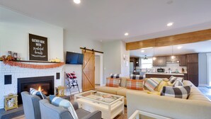 A modern living room with a fireplace, a sofa set, and a kitchen in the background. - Scenic Home on 20-acre Farm: Families Welcome (Cleveland)