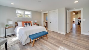 A bedroom with a large bed, a bench, a bedside table, a nightstand, a window, and a door leading to another room. - Scenic Home on 20-acre Farm: Families Welcome (Cleveland)