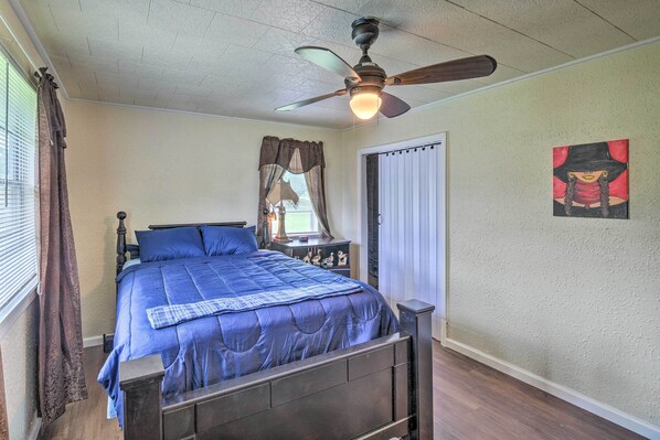 A bedroom with a bed, a ceiling fan, a window with curtains, and a door.