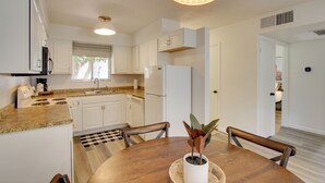 A modern kitchen with white cabinets, a granite countertop, a built-in stove, and a refrigerator. There is a dining table with chairs and a potted plant on it. - Walk to Papago Park: Condo w/ Community Perks! (Scottsdale)