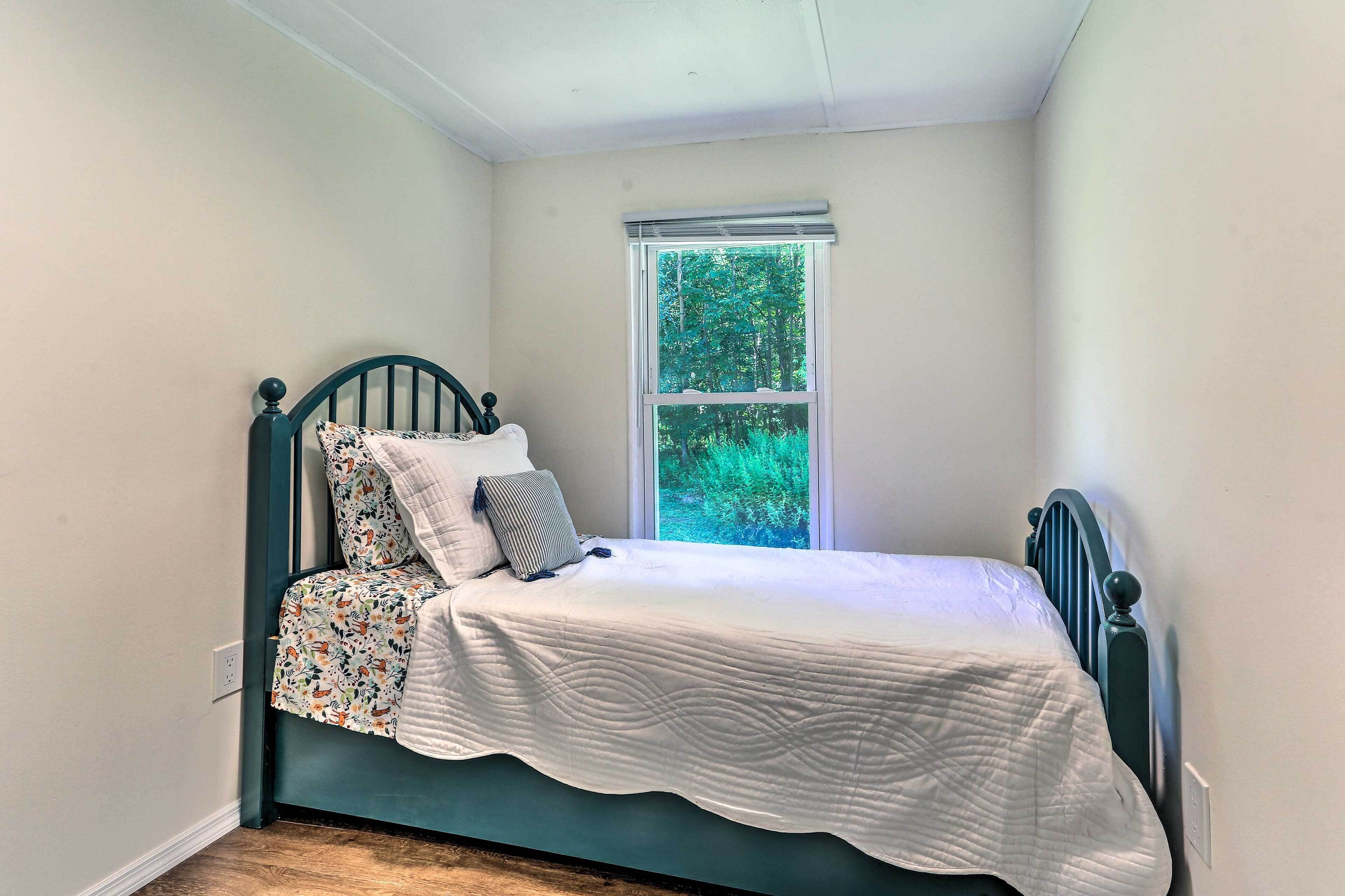 A small, single-bed room with a window, a bed with a patterned bedspread, and a plain wall.