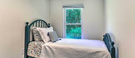A small, single-bed room with a window, a bed with a patterned bedspread, and a plain wall.