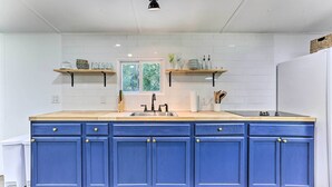 A kitchen with a wooden countertop, a sink, and blue cabinets. There are two windows above the sink, and a basket on the upper shelf. - Wallkill Riverfront Retreat: Canoe & Relax! (New Paltz)