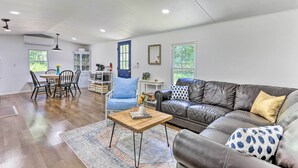 A spacious living room with a leather couch, a wooden coffee table, and a dining area with a blue chair and a wooden table. - Wallkill Riverfront Retreat: Canoe & Relax! (New Paltz)