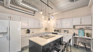 A modern kitchen with white cabinets, a central island with stools, and a hanging light fixture. - Dog-friendly Kingsland Rental on Lake Lbj! (Kingsland)