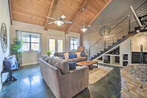 A spacious living room with a high ceiling, built-in wooden staircase, and a stone accent wall. - Dog-friendly Kingsland Rental on Lake Lbj! (Kingsland)