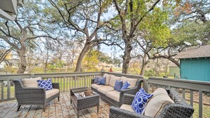 A covered outdoor seating area with wicker furniture and cushions, surrounded by trees and a view of the neighborhood. - Dog-friendly Kingsland Rental on Lake Lbj! (Kingsland)
