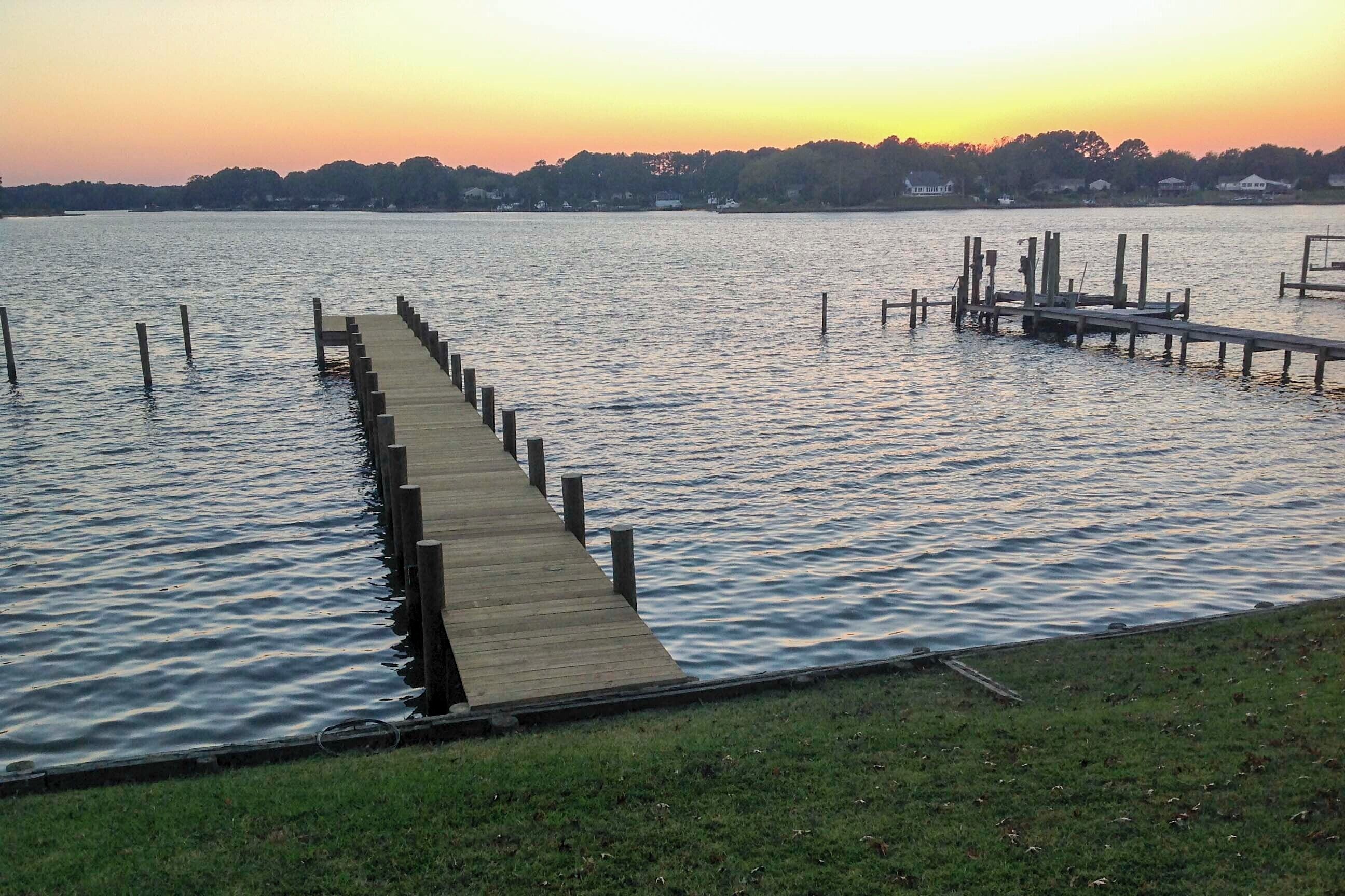 A wooden pier extending into calm water, surrounded by a grassy area.
