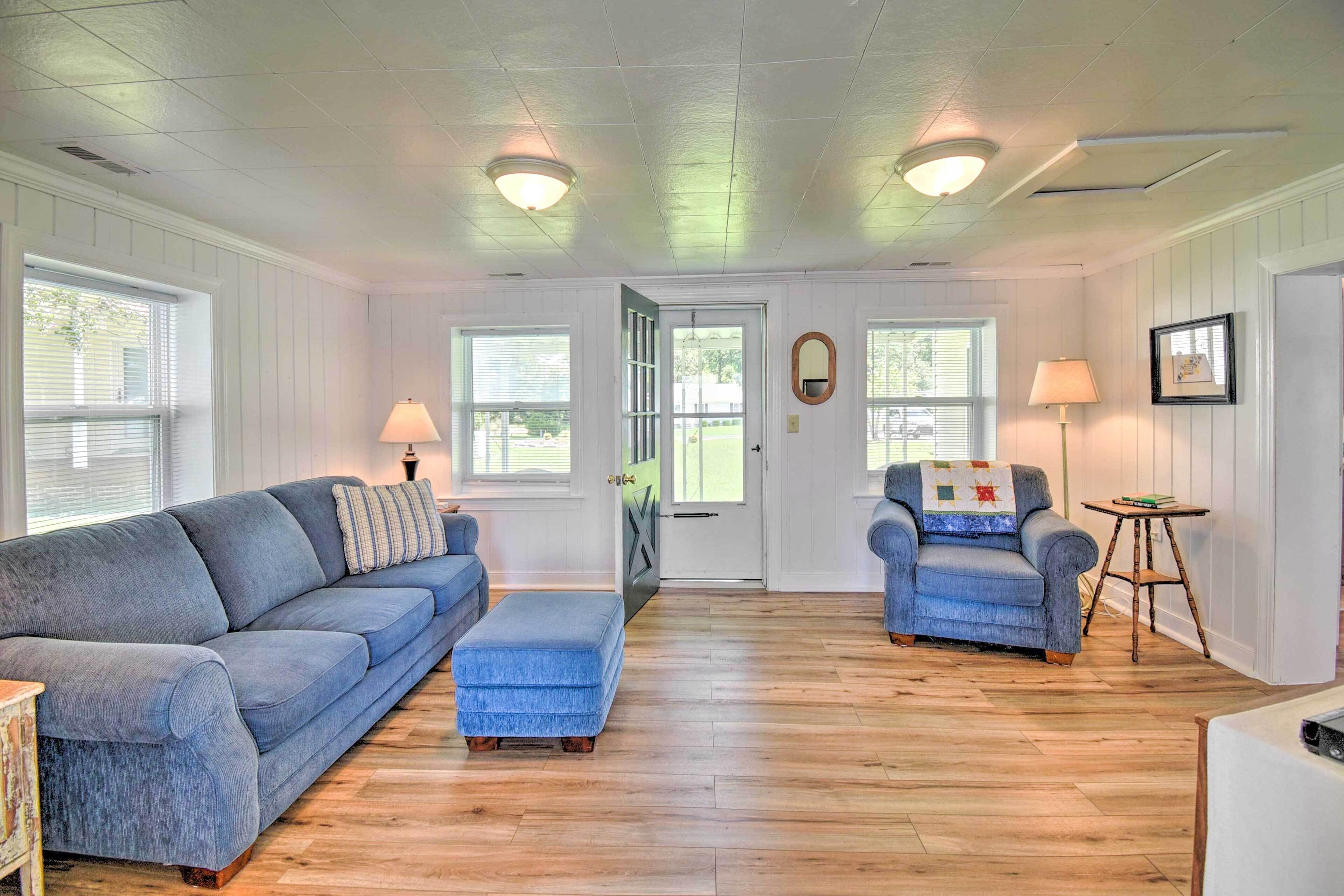 A room with a blue sofa, a matching ottoman, a blue armchair, and a small wooden table.