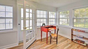 A room with large windows, a wooden desk, a chair, and a bookshelf. - Romantic Waterfront Abode With Patio & Dock! (Deltaville)