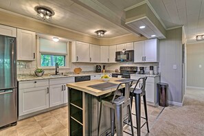 Una cocina moderna con armarios blancos, electrodomésticos de acero inoxidable y una zona de bar con taburetes.
