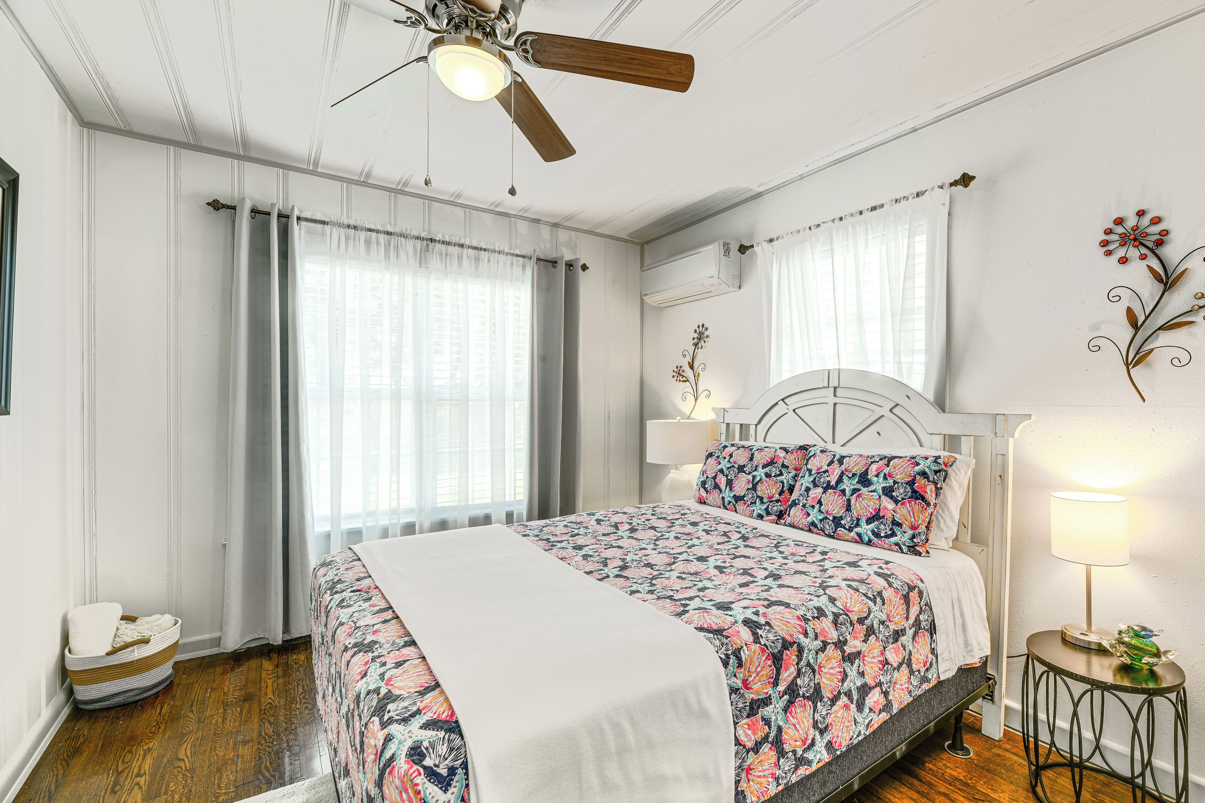 A bedroom with a bed, a ceiling fan, a bedside table with a lamp, and a decorative wall piece.