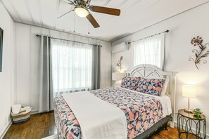 A bedroom with a bed, a ceiling fan, a bedside table with a lamp, and a decorative wall piece. - Cozy Cottage w/ Patio < 2 Mi to Rockport Beach! (Rockport)