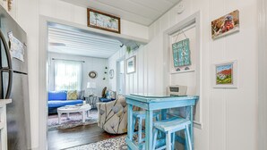 A hallway with a blue table and chairs, a sofa, and a dining table with chairs. There are framed pictures on the walls and a sign that says "Sandy to Sales & Successes".