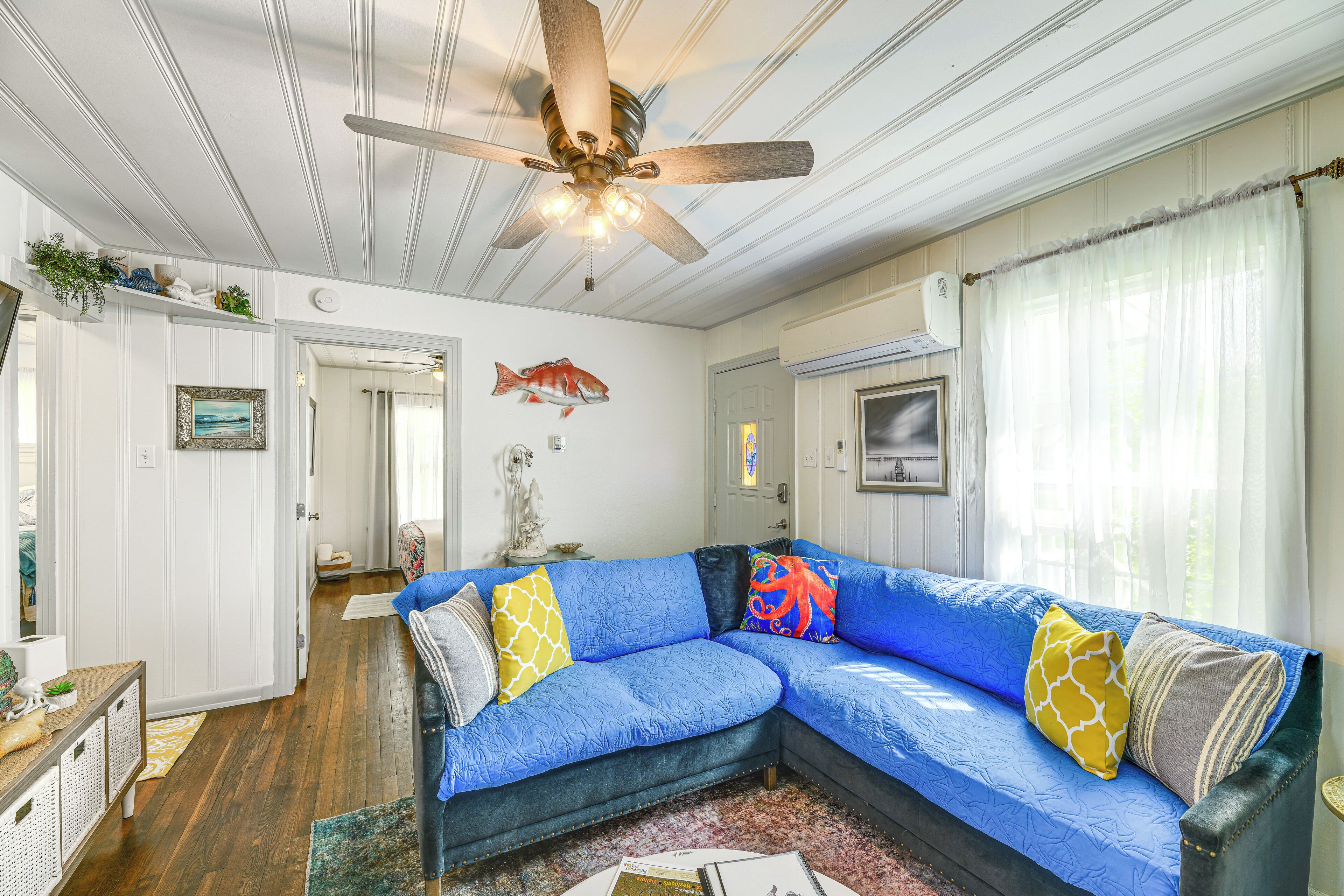 A living room with a blue sectional sofa, wooden ceiling fan, and a fish mural on the wall.