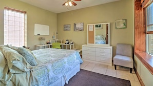 Quarto com cama, penteadeira, cadeira, escrivaninha, espelho e ventoinha no teto.