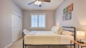 A bedroom with a bed, a desk, a chair, a ceiling fan, a window, and a door. - San Tan Valley Home w/ Pool Access & Golf View! (San Tan Valley)