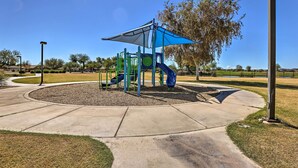 A playground with a slide and climbing structures, surrounded by a paved area and trees. - San Tan Valley Home w/ Pool Access & Golf View! (San Tan Valley)