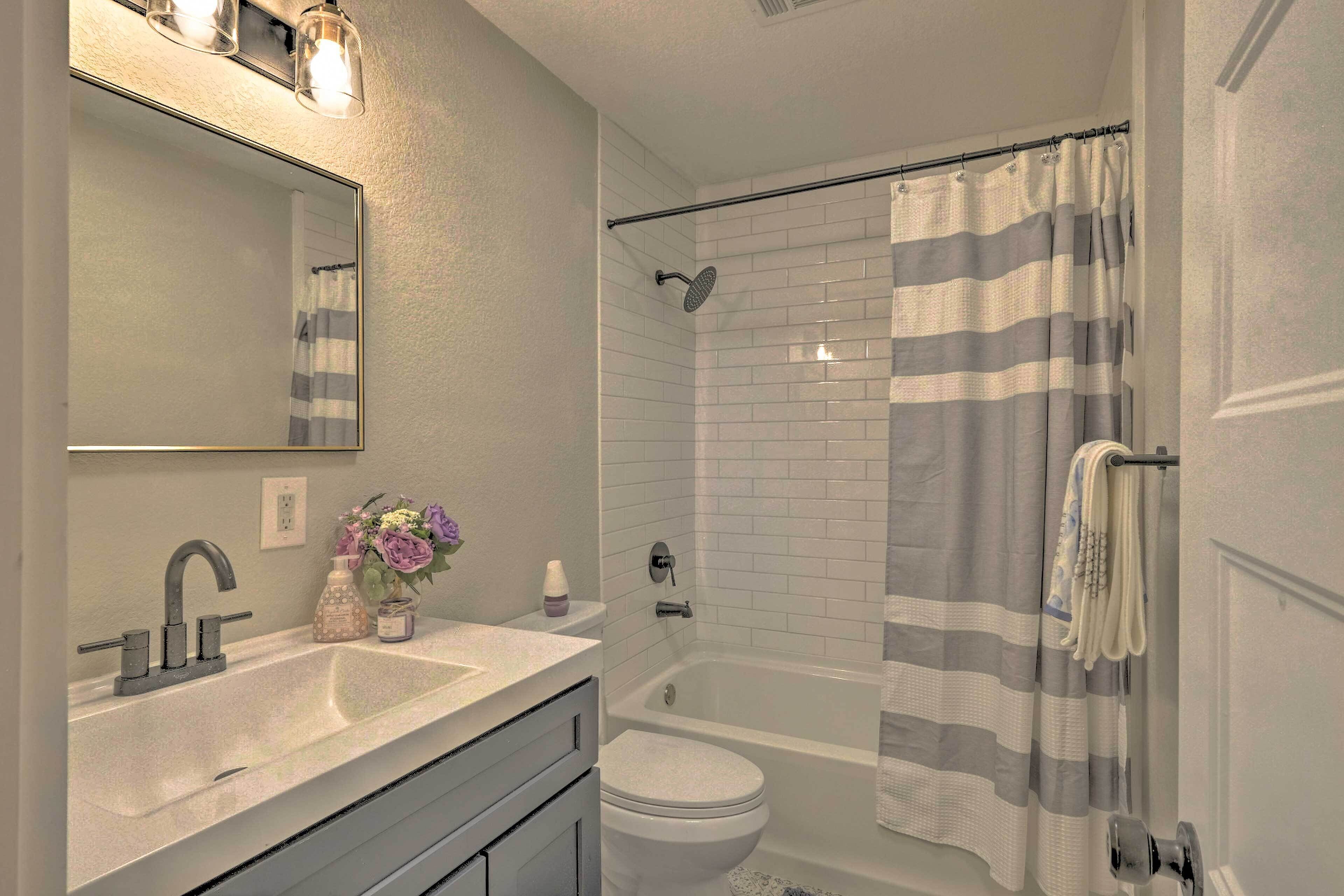 A bathroom with a sink, mirror, toilet, and a shower with a striped curtain.