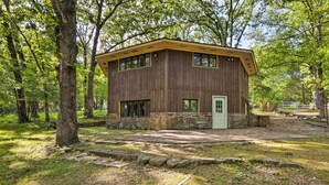 A rustic cabin with a stone foundation and wooden walls, surrounded by trees and a grassy area.