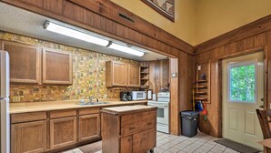 A kitchen with wooden cabinets, a countertop, a microwave, an oven, and a trash can.