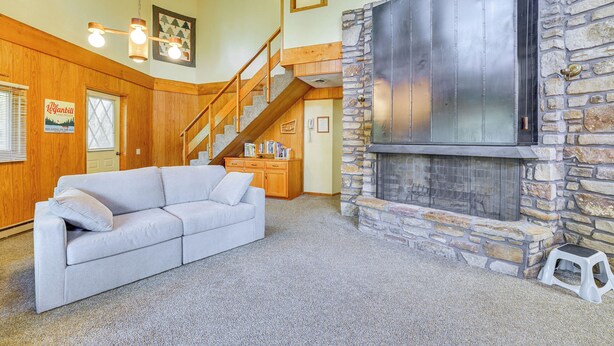 A living room with a stone fireplace, a wooden staircase, and a light-colored sofa.
