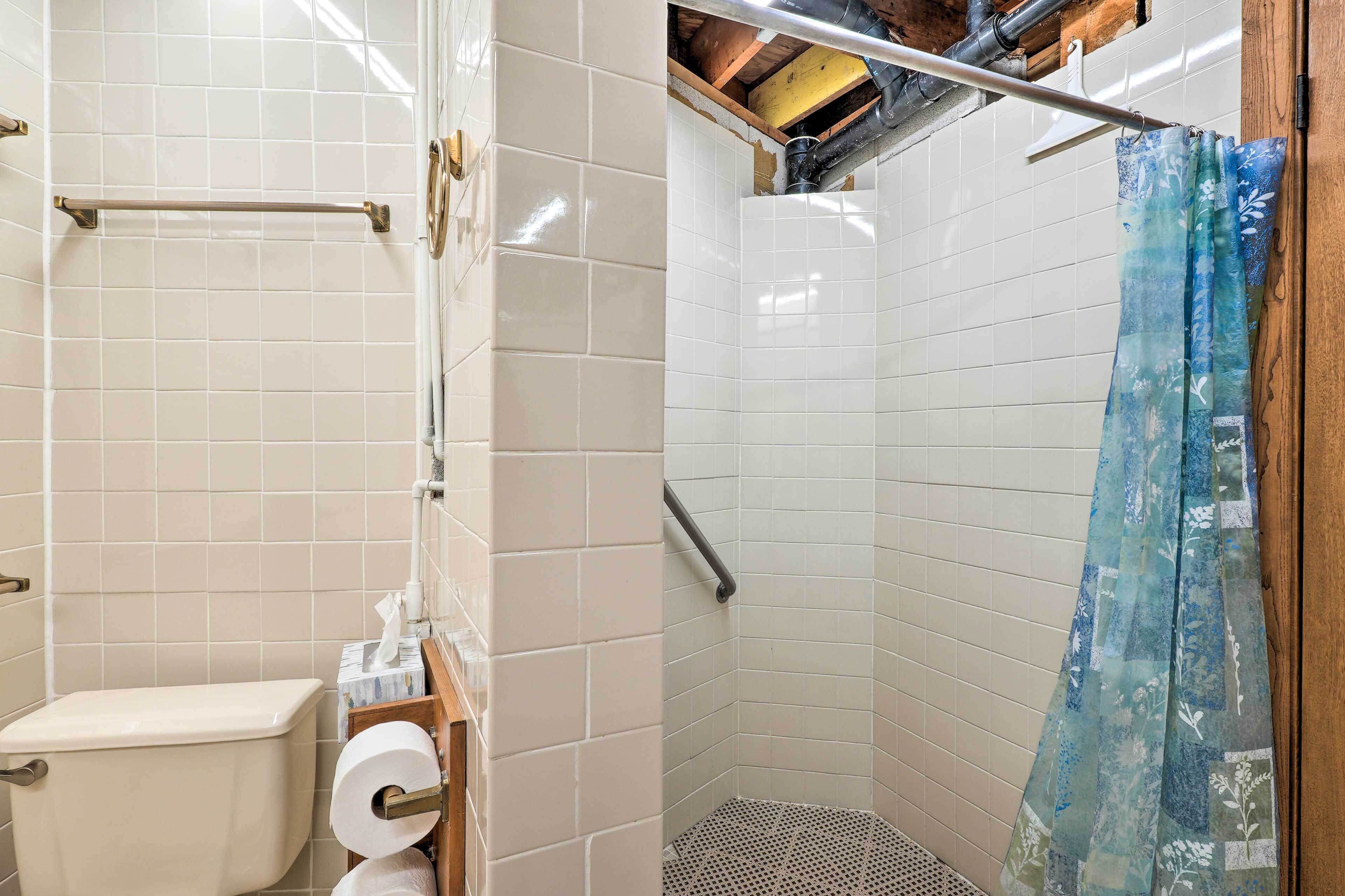 A bathroom with white tiled walls, a toilet, a roll of toilet paper, and a shower with a blue floral curtain.