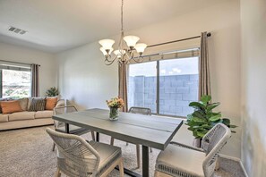 A dining area with a table and chairs, a chandelier, and a view of a brick wall outside. - Litchfield Park Home w/ Private Patio & Yard! (Litchfield Park)