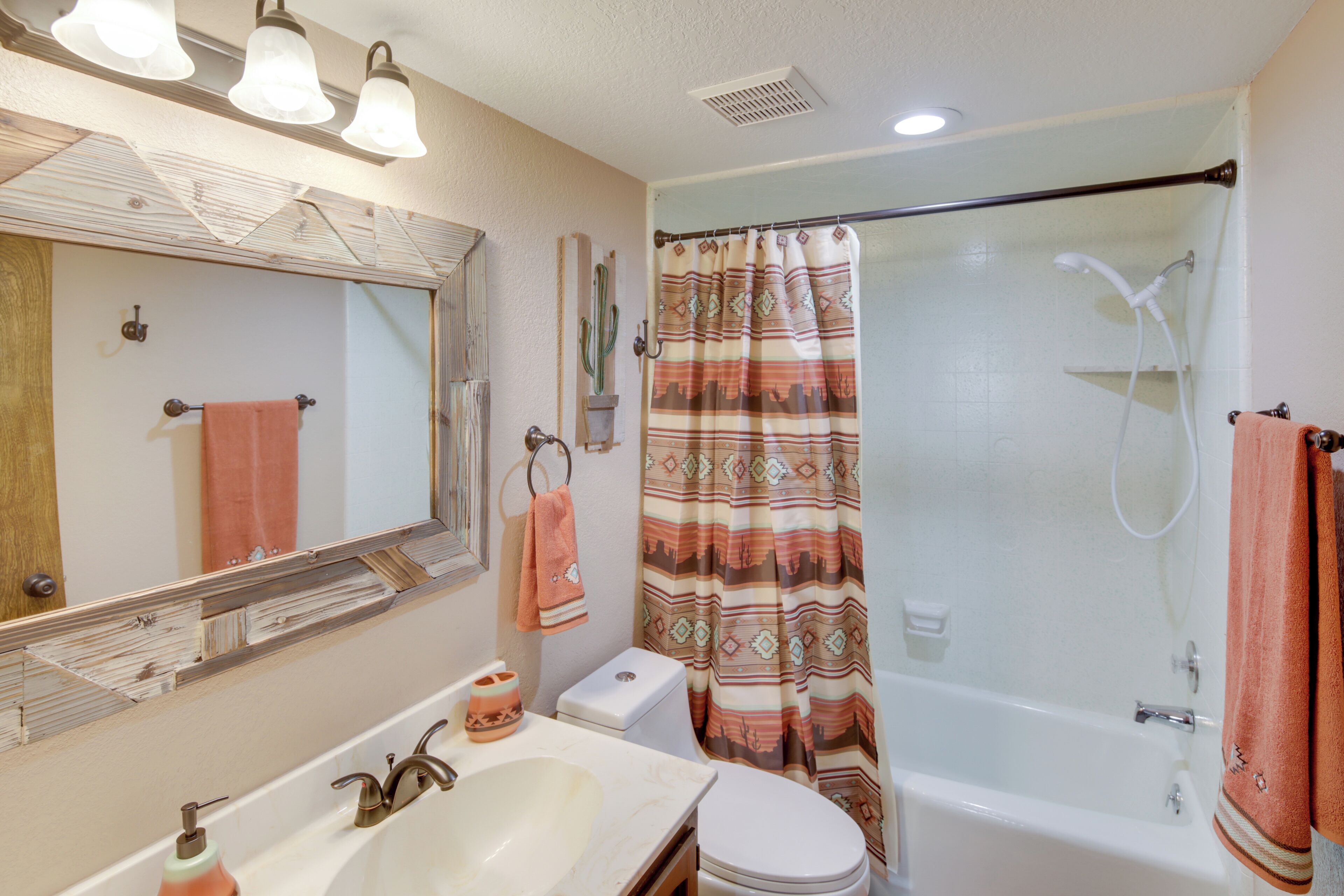Un baño con lavamanos, espejo, inodoro, ducha y cortina de baño estampada.