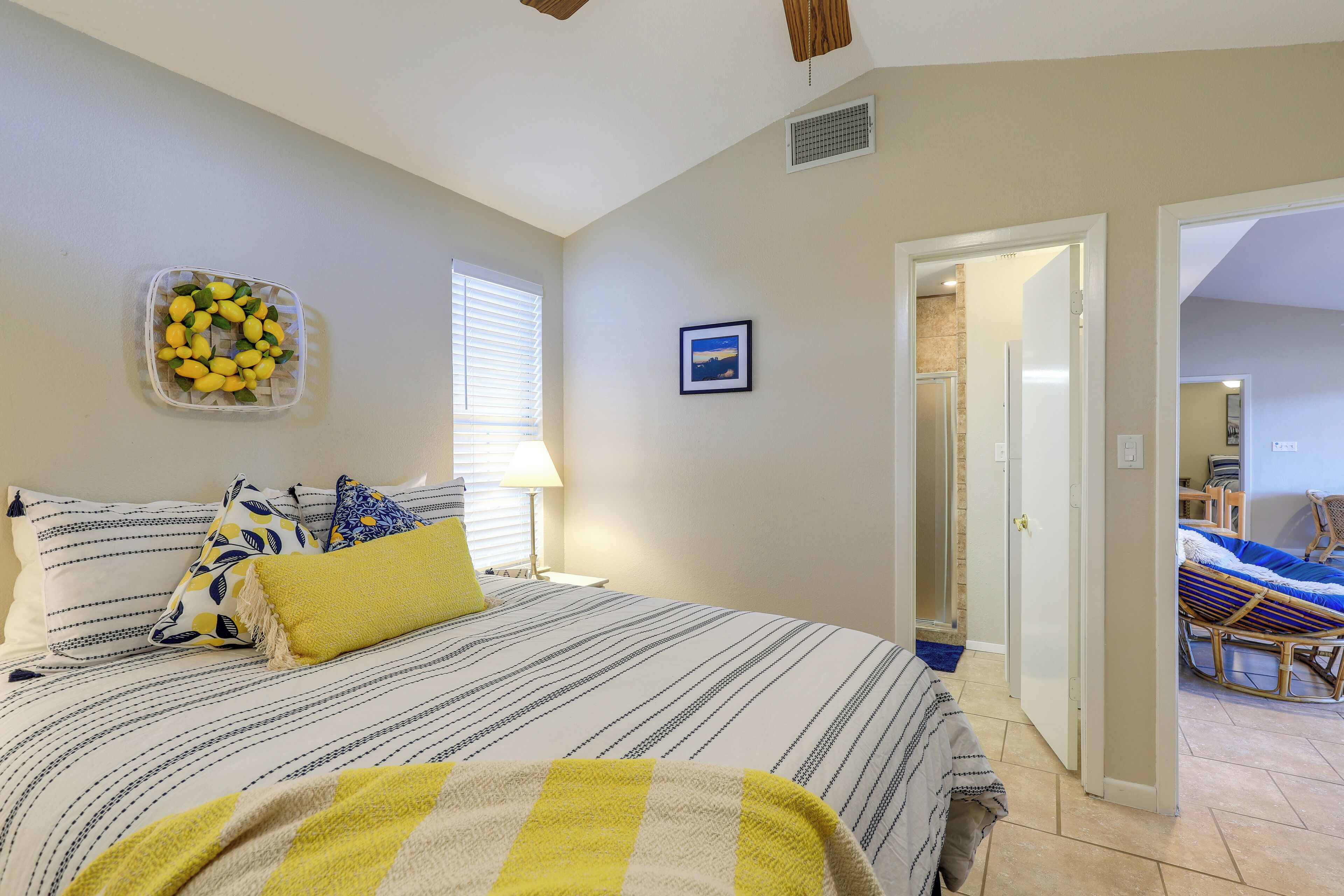 A bedroom with a bed, pillows, a bedside table, a lamp, a picture on the wall, and a door leading to another room.