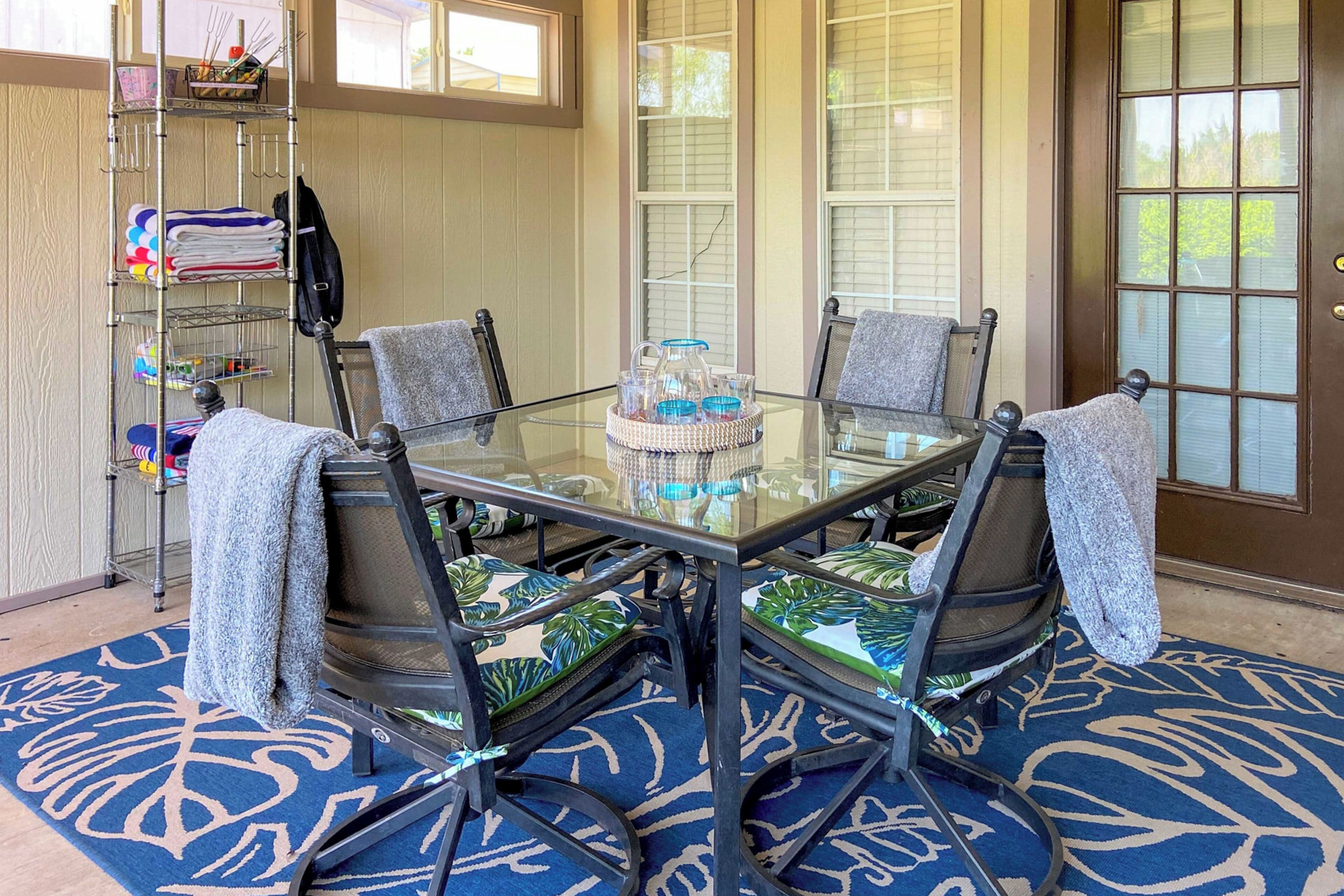 Een eethoek met een glazen tafel, vier stoelen en een blauw tapijt met een patroon.