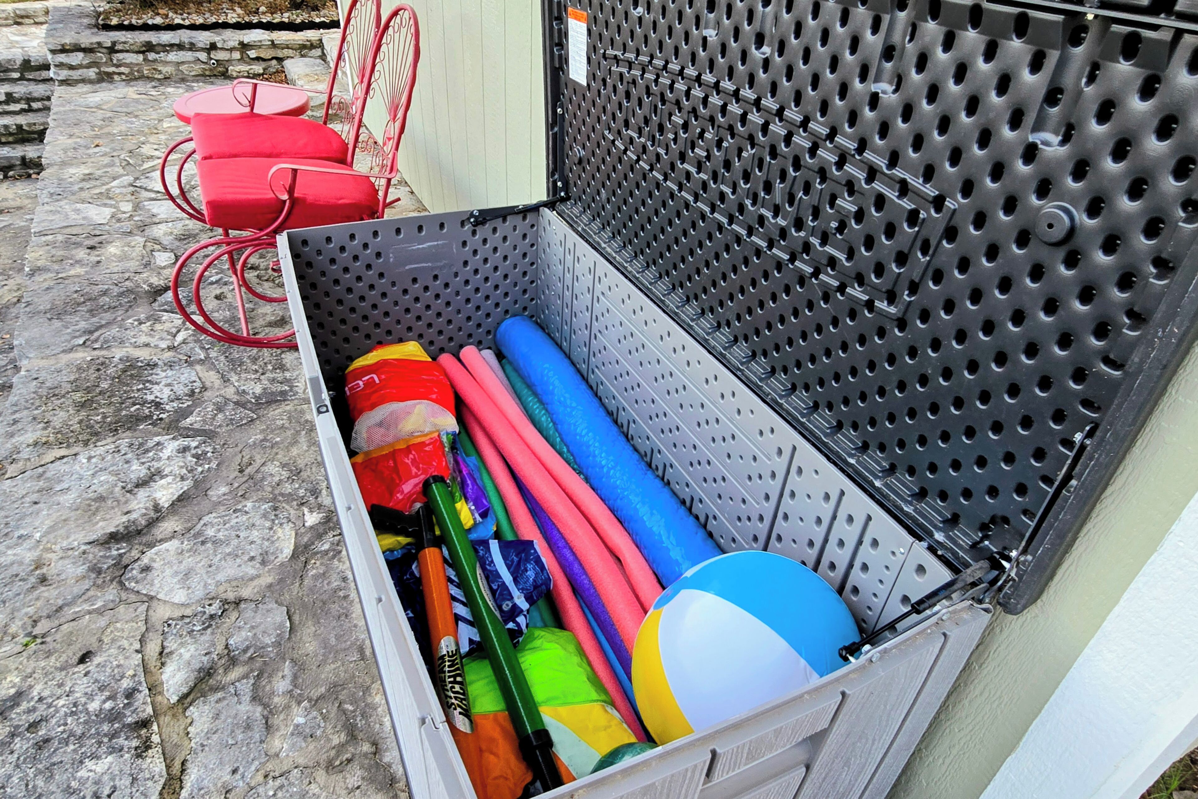 Un depósito de almacenamiento con varios equipos deportivos, incluyendo una pelota azul y amarilla, esterillas de colores y una silla roja.