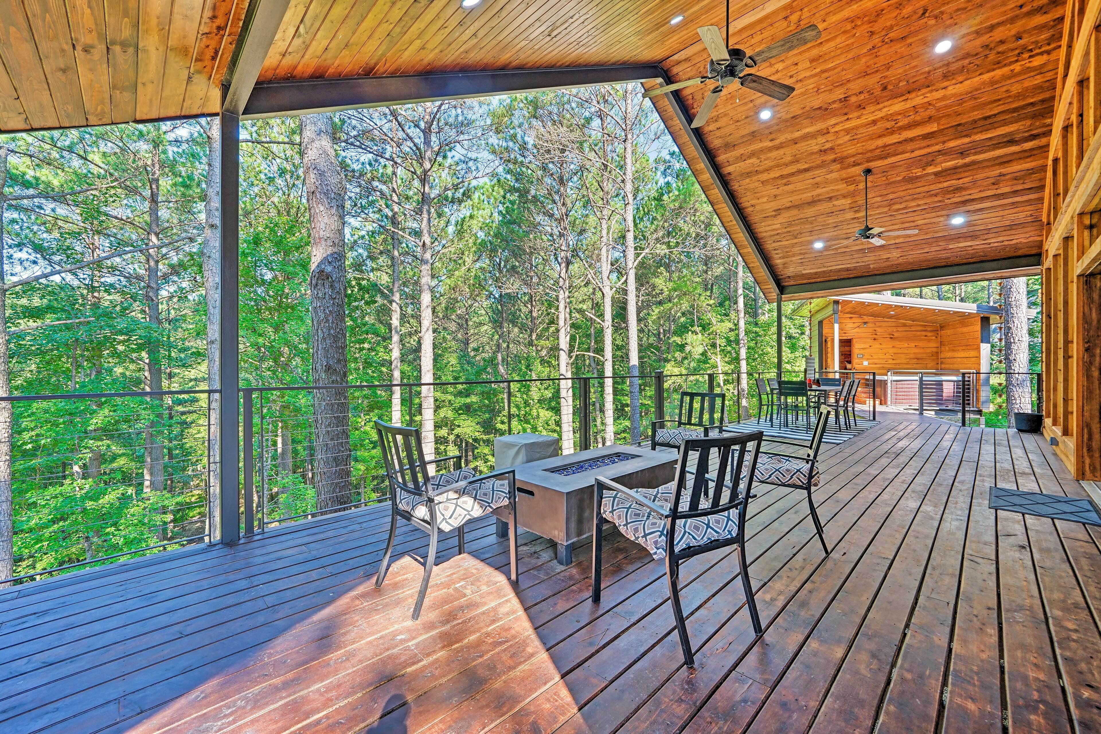 Una terraza de madera con mobiliario exterior, un ventilador de techo y vistas a un bosque.