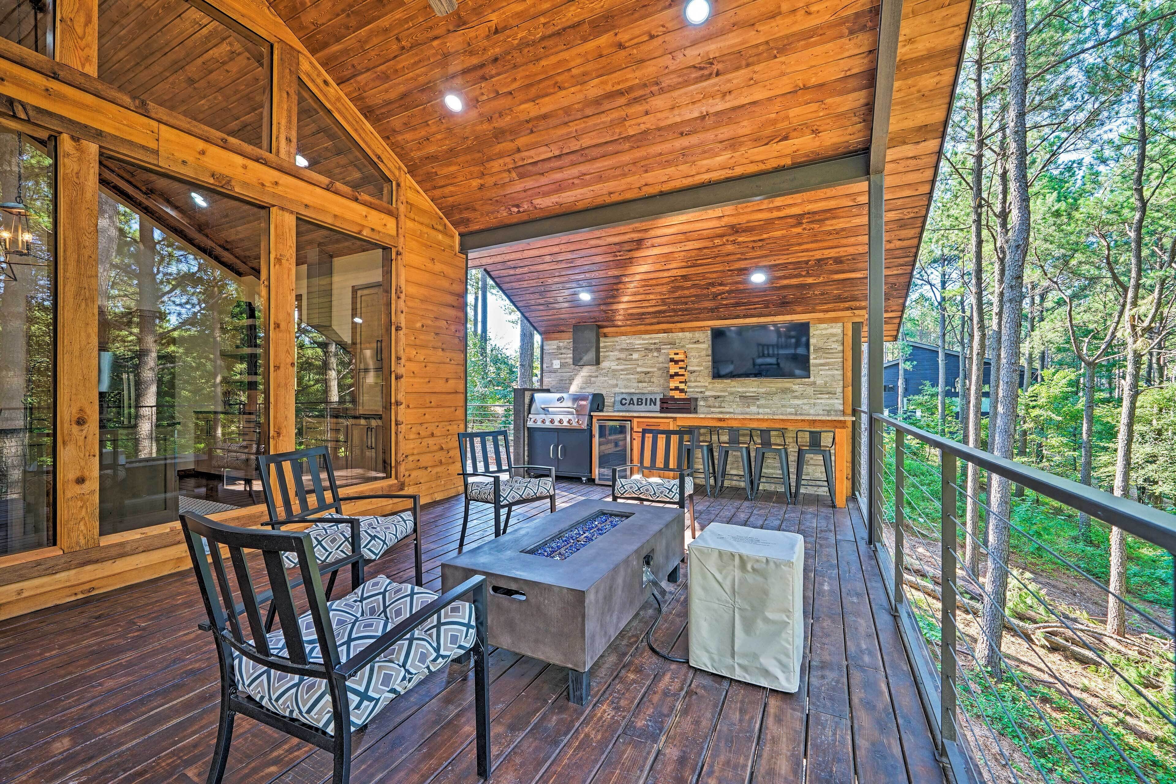A wooden deck with outdoor seating, a grill, and a stone fireplace.