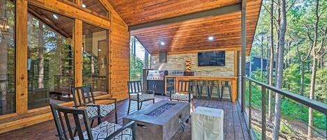 A wooden deck with outdoor seating, a grill, and a stone fireplace.