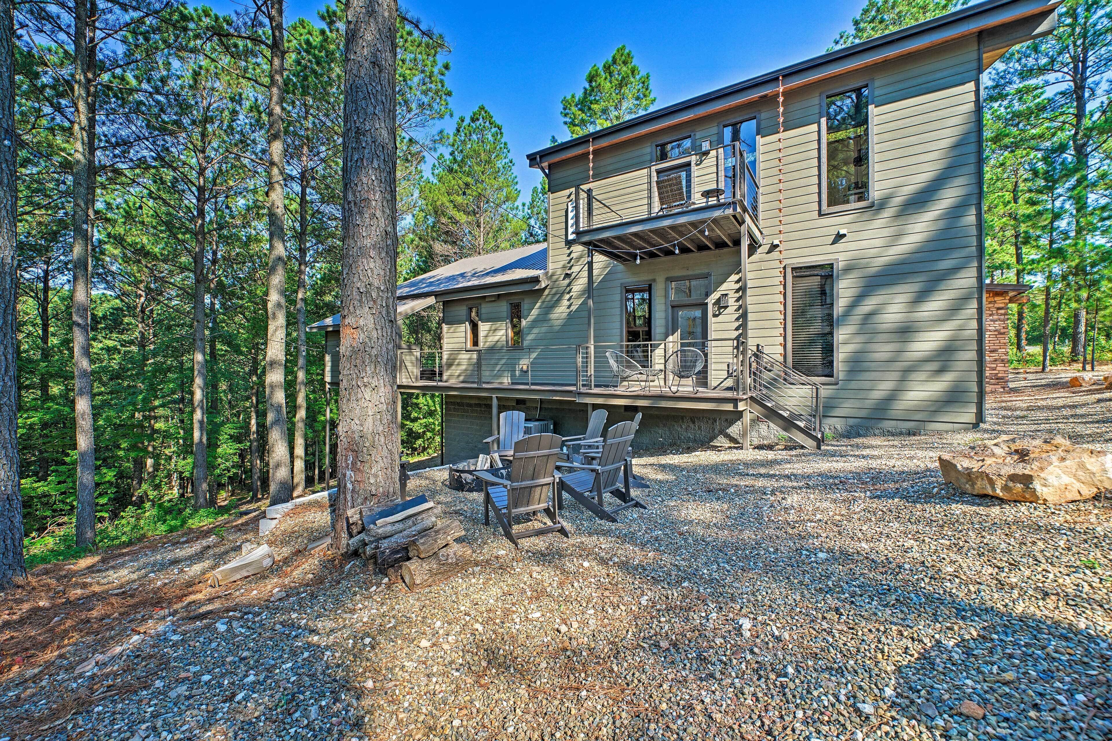 A two-story house with a deck, surrounded by a forest.