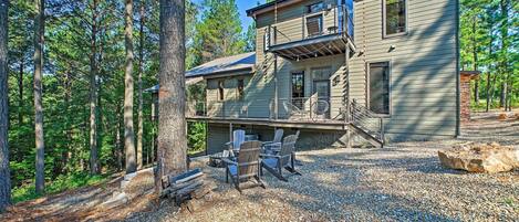 A two-story house with a deck, surrounded by a forest.